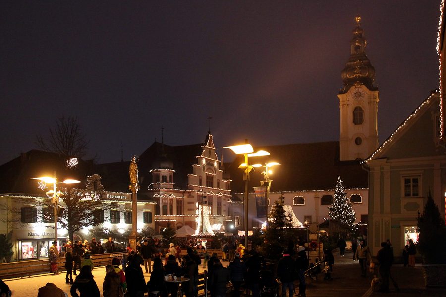 Hauptplatz di Hartberg illuminata con edifici storici, colonna mariana, municipio e chiesa parrocchiale di San Martino